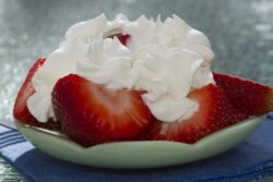 Sliced strawberries with whipped cream on a decorative green plate. They are served outdoors on a glass table