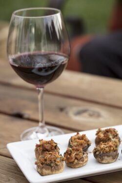 Sausage and Cheese baked stuffed mushrooms plated on white ceramic on a wood table and glass of wine