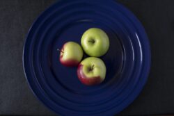 Three green and red crab apples on a blue plate as still life