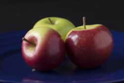 Three green and red crab apples on a blue plate as still life