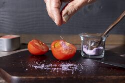 Chef salting a halved tomato on a wood cutting board