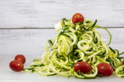 Spiralized Zucchini Noodles and Whole Miniature Tomatoes on a Cutting Board