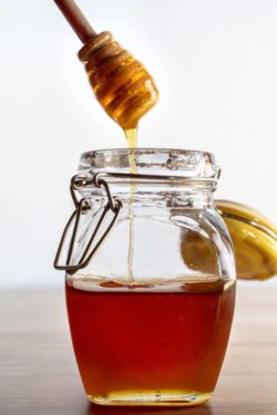 Stirring stick in a jar filling with golden sweet honey on a wood table top