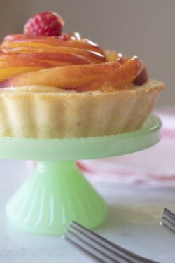 Miniature layered peach custard pie with a golden crust and served on a smal pedestal green plate, pink napkins and forks