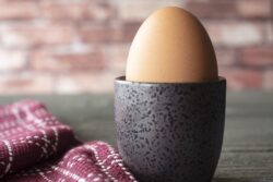 Soft boiled egg in a cup with a dish towel on a rustic table and brick background
