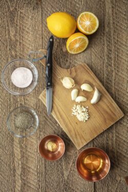 Ingredients consisting of salt, oil, garlic, pepper, and mustard for a dressing preparation on a chef's table with a cutting board