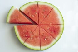 Watermelon sliced and cut into eight wedges on a white ceramic background