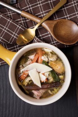 Bowl of colorful vegetable soup made of zucchini, carrots, meat, brussel sprouts, onions and chicken broth served with a brown napkin and gold spoon