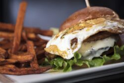 Plated hamburger with dressing, lettuce and a fried egg in a bun and crispy sweet potato fries on the side