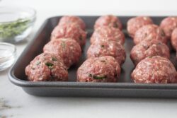 Raw meat balls prepared and ready to be baked on a sheet pan with seasonings on the side
