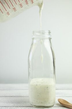 Homemade yogurt salad dressing being poured into a milk bottle