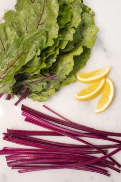 Fresh cut beet stems, leaves and lemon wedges on a marble cutting board