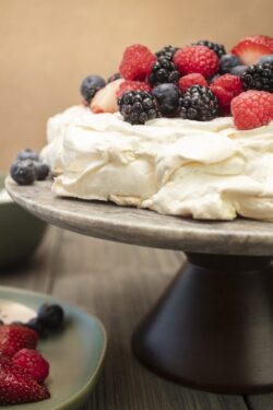 Pavlova meringue cake dessert made with strawberries, blackberries, raspberries and blueberries, planted on a granite platform