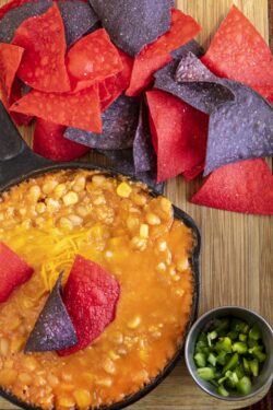 Mexican Chicken Chili made with corn and beans in a cast iron skillet, with red and blue tortilla chips and jalapeno peppers