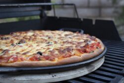 Pepperoni, cheese and tomato pizza being made on a cast iron skillet and on a barbeque grill outoors