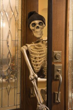 Halloween skeleton greeting at the door wearing a knitted hat