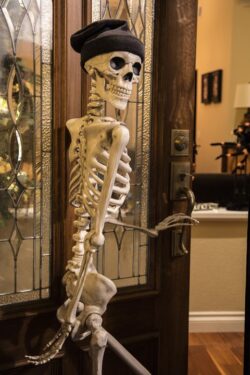 Halloween skeleton greeting at the door wearing a knitted hat
