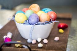Colored orange, purple, yellow, red and greed Easter eggs in a bowl with candy on the table top