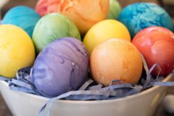 Colored orange, purple, yellow, red and greed Easter eggs in a bowl with candy on the table top