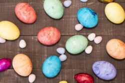 Colored blue, orange, green, red, purple and yellow Easter eggs laying on a wooden board surrounded by candy