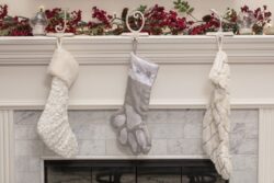 White Christmas stockings hanging from a fireplace mantel with green and red garland, and lights above